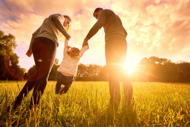 Parents holding a baby's hands while walking in a field at evening